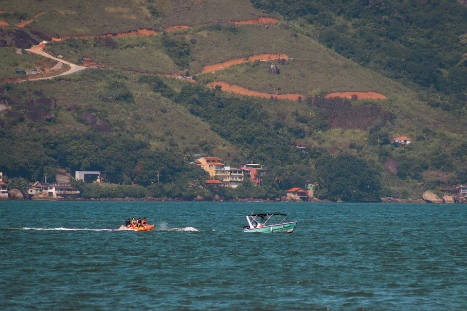 barcos no mar com casas e morros ao fundo