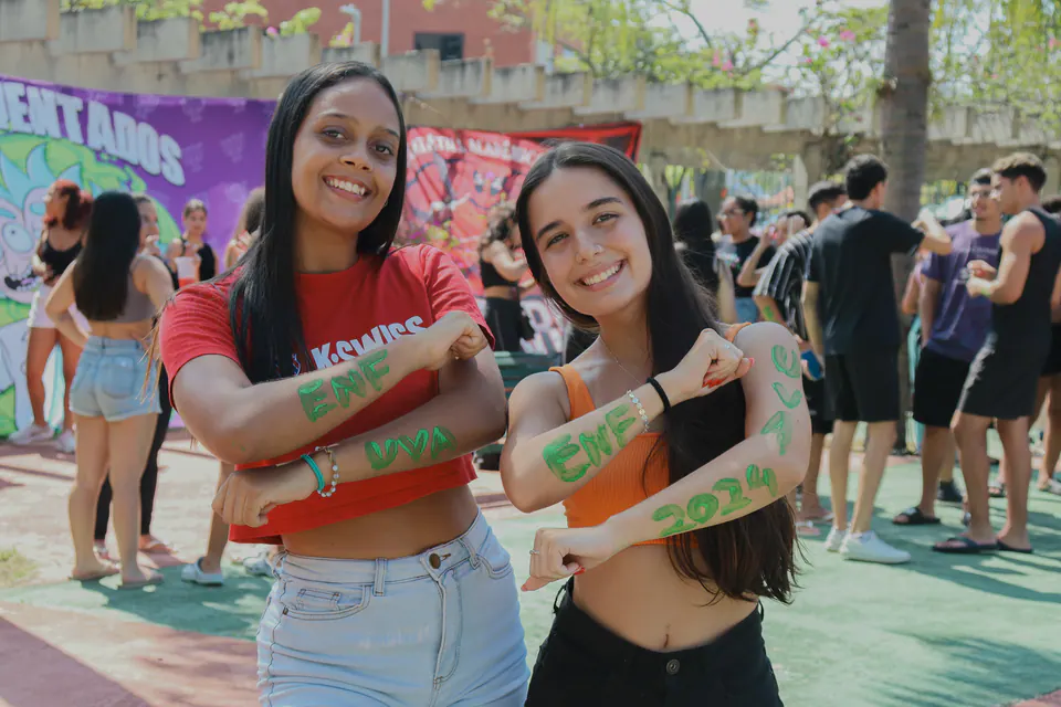 duas calouras cruzam os braços pintados em frente às bandeiras