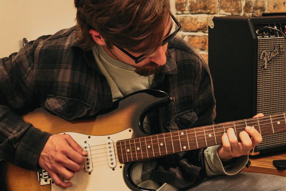 hugo motta tocando guitarra em plano fechado, com o amplificador ao fundo